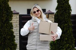 Courier showing thumbs up while holding cardboard boxes in front of a house photo