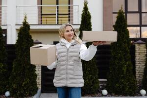 Delivery woman holding two cardboard boxes in front of a house photo