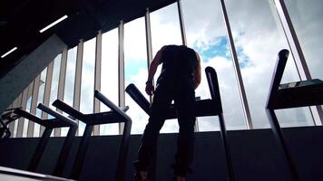 Sportsman on treadmill in gym. Guy in sportswear standing on a treadmill and doing running exercise on window background. Back view from below. video