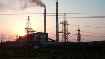 Panoramic view on harmful power station at sunset. Tall electricity pylons next to large factory with smoke stacks on the evening sky. Camera rising up. video