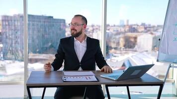 Astonished businessman at workplace. Smiling office worker sitting at the table with a laptop on window background with city view. video