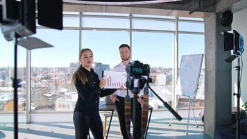Young woman recording in front of camera. Business people standing in office center and talking about projects on camera on large windows background. video