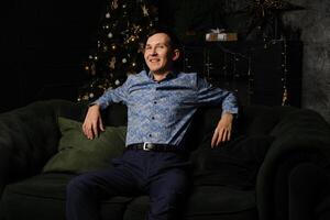 A Happy Man is Relaxing on a Comfortable Couch Surrounded by a Beautiful Christmas Tree photo