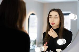 Woman Applying Lip Gloss While Looking in the Mirror photo