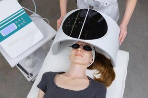 Beautician using led light therapy facial device on client for skin rejuvenation photo