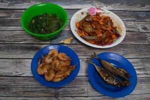 Traditional food with spicy shrimp, fried fish and stir-fried vegetables served on a rustic table. photo