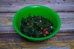 Stir-fried cassava shoots and chilies served in a green bowl on a rustic wooden background. photo
