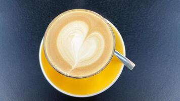 Cup of coffee with heart shape latte art on yellow saucer on dark cafe table photo
