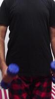 A man lifting dumbbells for bicep curls, dressed in a black t-shirt and red plaid pants-exercise sequence in progress. video