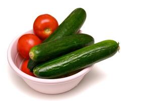 Bright red tomatoes and crisp cucumbers in a ceramic bowl on a table, prepared for a healthy fresh salad. photo