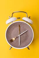 Empty plate with utensils in the form of clock hands as a conceptual background for lunch time photo