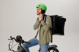 Delivery rider prepares for work while sitting on bicycle with backpack full of orders in studio setting photo