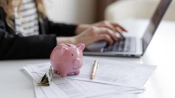Managing personal finances with a laptop, piggy bank, and documents at a desk during daylight hours photo
