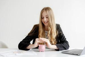 Young woman smiling while saving money in a pink piggy bank at a desk with documents and a laptop during a productive work session photo