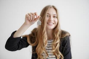 Smiling young woman holds keychain while showing excitement for new beginnings in a bright, minimalistic setting photo