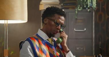The man dials a number on a wired phone and starts talking. He's sitting in a retro office. photo