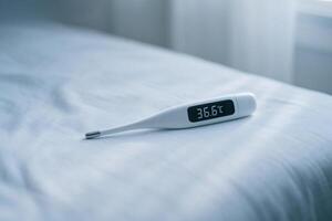 Digital thermometer on bed with 36.6 C reading, home healthcare, fever check and wellness monitoring with copy space photo
