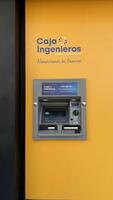 Malaga, Spain, May 18, 2025. ATM machine from Caja Ingenieros is displayed on a yellow wall, modern banking solutions and accessibility for users in urban settings focused on financial services photo