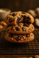 A delicious stack of three chocolate chip cookies, one with a bite taken, revealing a gooey center and nuts, on a cooling rack photo