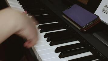 A woman plays an electronic piano based on notes recorded in her phone and on a piece of paper. Close-up of a piano and female hands video