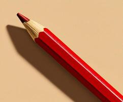 Red pencil on beige background with shadow. photo