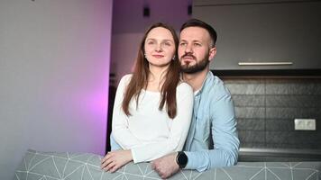 Romantic valentine portrait couple embracing tenderly, contemporary and woman reclining on ambient sofa, illuminated by soft purple man lighting in minimalist home interior video