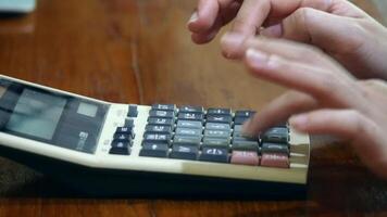 A hand pressing buttons on a vintage calculator with a wooden desk background, showing close-up details of keys and display video