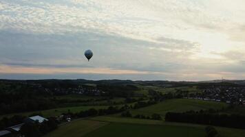 Shot of a hot air balloon in the sky flying over neat village houses nestled in a green forest. Aero shooting in the evening, Germany. photo