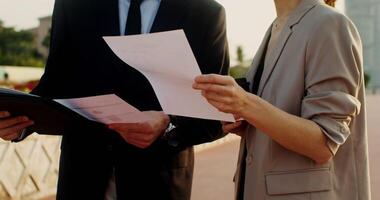 Man and a woman in business clothes are studying documents, talking with a serious look, standing on the street of a modern city photo