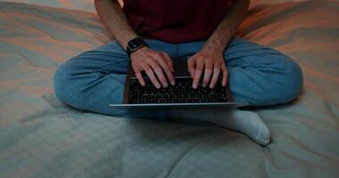 Man is typing on a laptop, sitting in a lotus position on the bed, Close-up of male hands on the keyboard, no face, front view from above photo