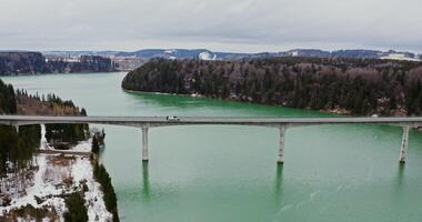 Concrete bridge for road transport across a wide river in a picturesque place among forests and fields covered with snow, drone , from the side of the river photo