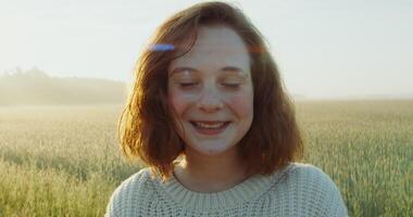 Rd-haired woman laughs while looking at the camera while walking through a wheat field in the bright light of the rising sun. Nice young face, close-up. 4k , red komodo photo