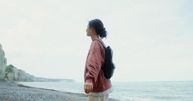 Woman smiles and spins around herself, enjoying the sea breeze, standing on the coast near the chalk cliffs. Etretat, France. 4k , red komodo photo