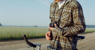 A young stylishly dressed man takes photographs with a camera while standing near a picturesque wheat field on a sunny day photo