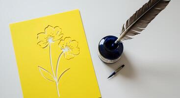 A yellow card with a flower on it next to a pen and a feather photo