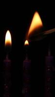 Single match flame gradually ignites multiple candles in sequence on black background video