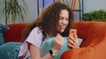 Happy young woman at home use smartphone typing browsing wow yes found out great big win celebrate video
