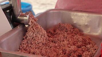 Fresh minced meat being dispensed into a metal tray from an electric grinder during food preparation. Great for visuals focused on meat processing, culinary production, or butcher work. video