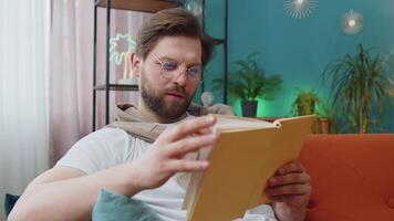 Young man relaxing interesting book turning pages smiling enjoying literature taking a rest on sofa video