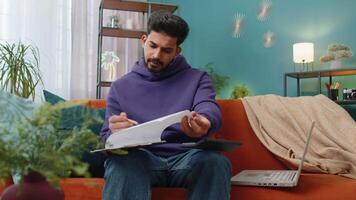 Indian man freelancer work with documents from home, analyzing information prepare financial report video