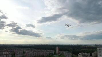 A hovering drone takes off against a cloudy sky and forest background. The quadcopter is flying towards the forest and residential area of the city video