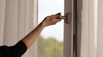 A person reaches for the window handle to open it, inviting fresh air into the cozy room. Natural sunlight brightens the space, creating a serene atmosphere video
