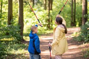 woman and son lifting their Nordic walking poles overhead during a sunny forest hike, enjoying active family time photo