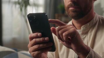 Man using mobile phone at home scrolling gadget screen shopping online technology reading social media in apartment male buyer consumer guy browsing smartphone internet store delivery cropped view video
