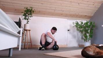 man training with kettlebell at home while working from the computer from home, performing workout between working sessions, petting his dog video