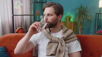 Thirsty Caucasian man sitting at home holding glass of natural aqua make sips drinking still water video