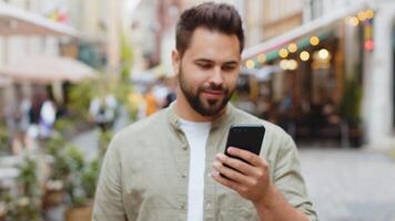 Young man use smartphone typing text messages browsing internet finishing work looking at camera video