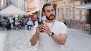 Young man use smartphone typing text messages browsing internet finishing work looking at camera video