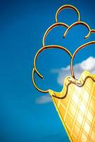 Retro neon ice cream cone sign against a vibrant blue sky with a hint of cloud photo