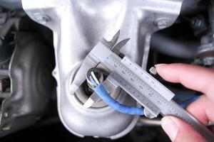 Vernier Caliper, A close up of a person hand holding and using a vernier caliper to measure a metal object. photo